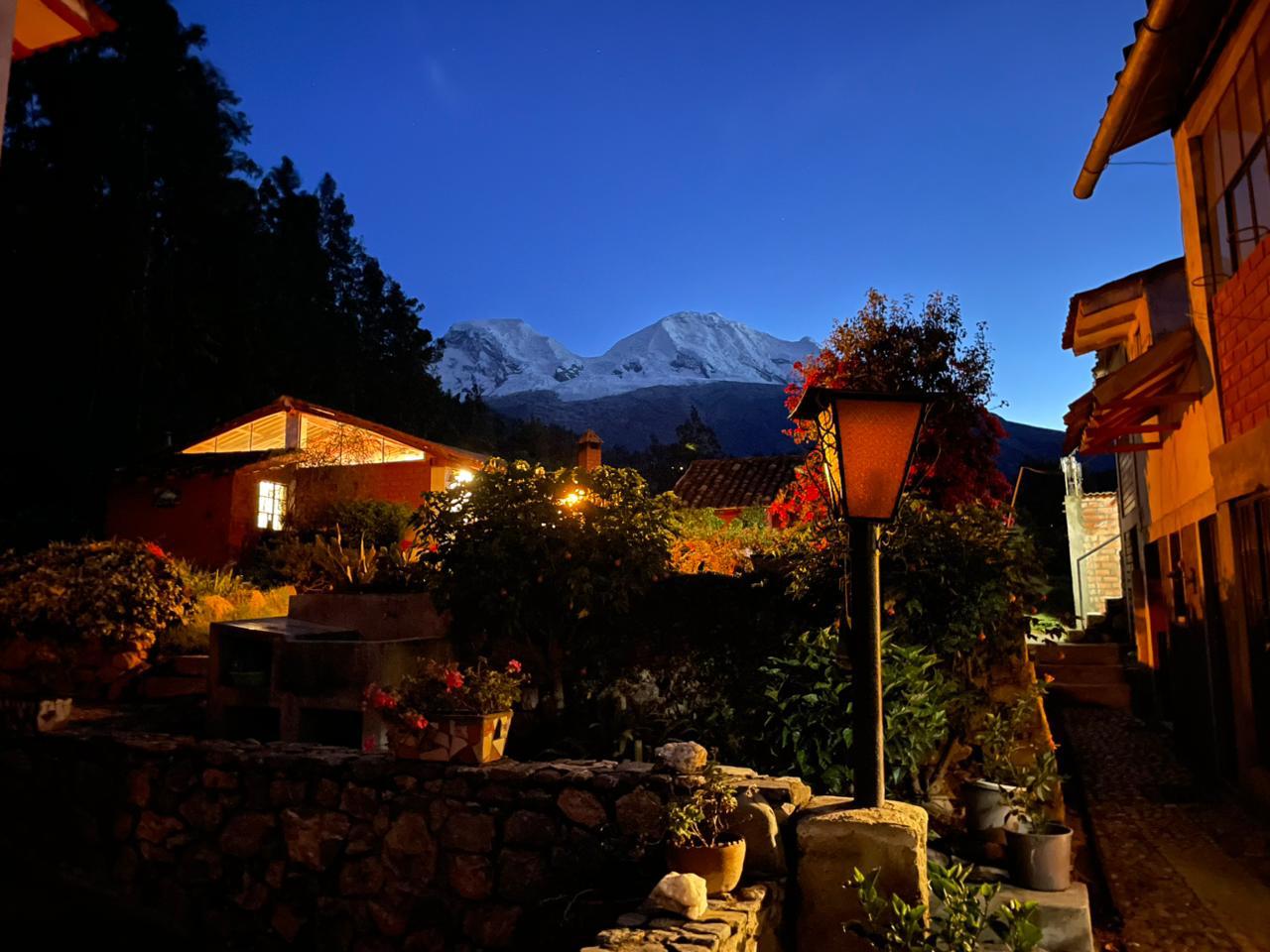 La Casita in Mancos at dusk: garden lantern and stone wall lit, snow-capped peaks of the Cordillera Blanca behind